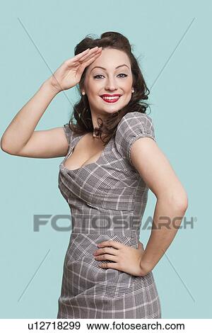 Stock Photo - Portrait of beautiful young woman in dress saluting against blue background. Fotosearch