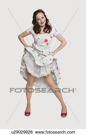 Stock Photograph - Portrait of beautiful young woman in dress with hands on hips against white background. Fotosearch