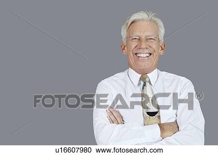 Stock Image - Portrait of cheerful senior businessman with arms crossed over gray background. Fotosearch