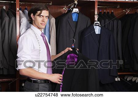 Portrait of confident man holding new suit in store View Large Photo Image Stock Photo - Portrait of confident man holding new suit in store. Fotosearch