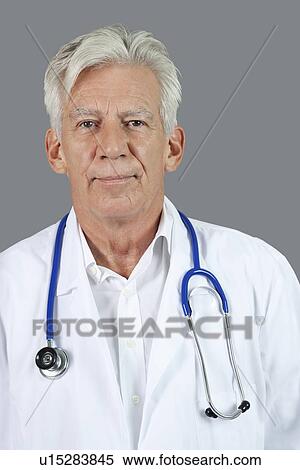 Stock Photography - Portrait of confident senior doctor with stethoscope around neck over gray background. Fotosearch