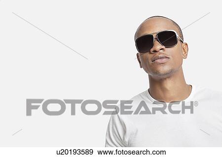 Portrait of confident young man wearing sunglasses against white background View Large Photo Image Stock Photo - Portrait of confident young man wearing sunglasses against white background. Fotosearch