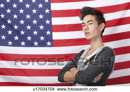 Portrait of confident young man with arms crossed standing against American flag View Large Photo Image Picture - Portrait of confident young man with arms crossed standing against American flag. Fotosearch