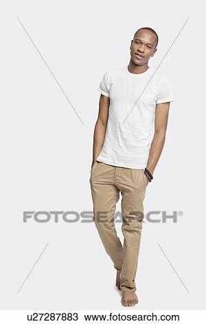Stock Image - Portrait of confident young man with hands in pockets against white background. Fotosearch