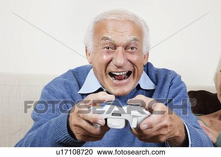 Portrait of excited elderly man playing video game at home View Large Photo Image Stock Image - Portrait of excited elderly man playing video game at home. Fotosearch