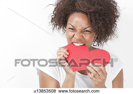 Portrait of frustrated young African American woman biting heart shape against white background View Large Photo Image Stock Photo - Portrait of frustrated young African American woman biting heart shape against white background. Fotosearch