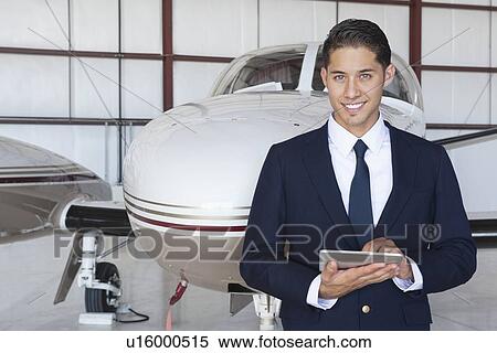 Portrait of handsome young pilot using tablet PC in front of airplane View Large Photo Image Stock Photography - Portrait of handsome young pilot using tablet PC in front of airplane. Fotosearch