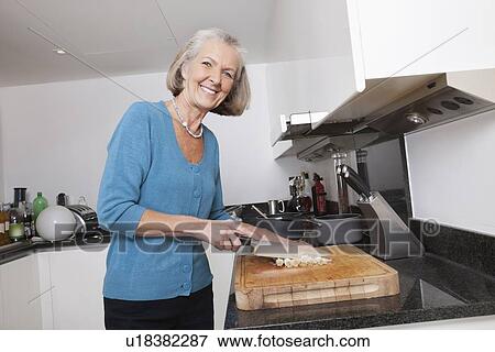 Portrait of happy senior woman chopping vegetables at kitchen counter View Large Photo Image Stock Photo - Portrait of happy senior woman chopping vegetables at kitchen counter. Fotosearch