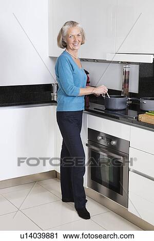 Stock Image - Portrait of happy senior woman preparing food in kitchen. Fotosearch