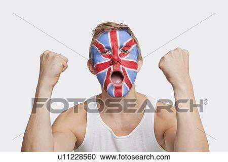 Stock Image - Portrait of happy young Caucasian man with British flag painted on face celebrating success against white background. Fotosearch
