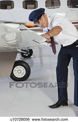 Stock Photograph - Portrait of happy young male pilot inspecting airplane's wing. Fotosearch