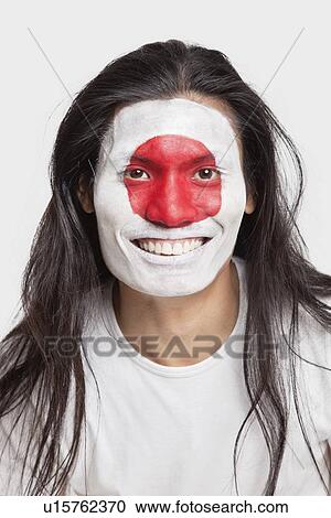 Stock Image - Portrait of happy young man with long hair and Japanese flag painted on face against white background. Fotosearch