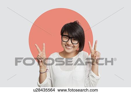 Picture - Portrait of happy young woman gesturing peace sign against Japanese flag. Fotosearch