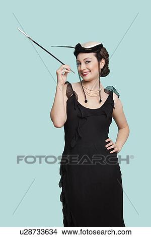 Portrait of happy young woman in black dress holding old-fashioned cigarette holder against blue background View Large Photo Image Picture - Portrait of happy young woman in black dress holding old-fashioned cigarette holder against blue background. Fotosearch