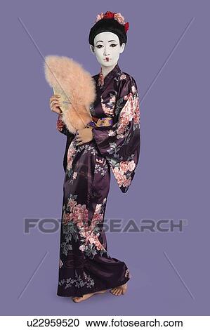Stock Image - Portrait of Japanese woman in kimono holding folding fan against purple background. Fotosearch