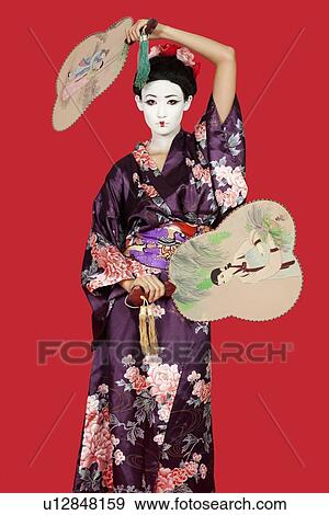 Portrait of Japanese woman in kimono holding fans standing against red background View Large Photo Image Stock Photo - Portrait of Japanese woman in kimono holding fans standing against red background. Fotosearch