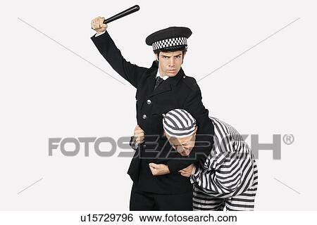 Stock Photograph - Portrait of police officer with nightstick arresting male prisoner against gray background. Fotosearch