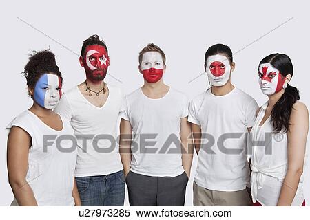 Stock Photography - Portrait of serious Multi-ethnic group of friends with various national flags painted on their faces standing against white background. Fotosearch