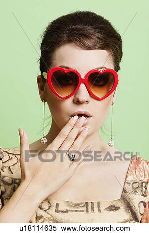 Portrait of shocked young woman wearing heart shaped sunglasses against green background View Large Photo Image Stock Photography - Portrait of shocked young woman wearing heart shaped sunglasses against green background. Fotosearch