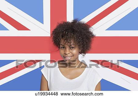 Stock Photo - Portrait of young African American woman in white t-shirt smiling against British flag. Fotosearch