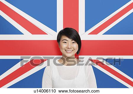 Stock Image - Portrait of young Asian woman smiling against British flag. Fotosearch