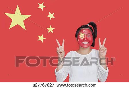 Stock Photo - Portrait of young Asian woman with painted face gesturing peace sign against Chinese flag. Fotosearch