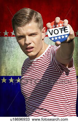 Stock Image - Portrait of young Caucasian man displaying vote badge standing outdoors. Fotosearch