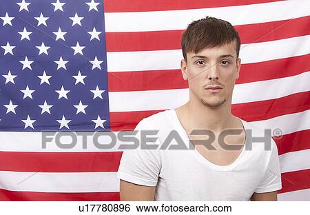 Stock Photograph - Portrait of young Caucasian man standing against American flag. Fotosearch
