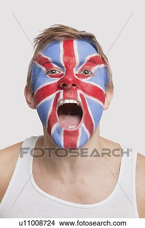 Picture - Portrait of young Caucasian man with British flag painted on face cheering against white background. Fotosearch