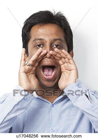 Stock Photograph - Portrait of young Indian man shouting against white background. Fotosearch