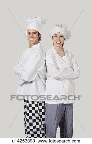 Stock Image - Portrait of young man and woman in chef's uniform with arms crossed against gray background. Fotosearch