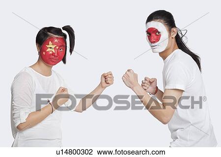 Stock Image - Portrait of young man and woman with Asian flags painted on face holding up their fists to fight against white background. Fotosearch