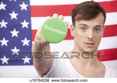 Portrait of young man displaying volunteer badge against American flag View Large Photo Image Stock Photo - Portrait of young man displaying volunteer badge against American flag. Fotosearch