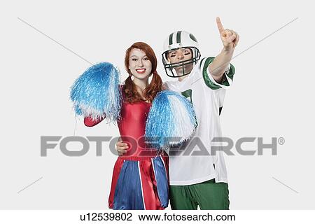 Portrait of young man in football uniform and cheerleader with pom-pom standing over gray background View Large Photo Image Stock Image - Portrait of young man in football uniform and cheerleader with pom-pom standing over gray background. Fotosearch