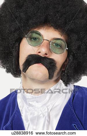 Portrait of young man wearing wig and mustache against gray background View Large Photo Image Stock Photograph - Portrait of young man wearing wig and mustache against gray background. Fotosearch