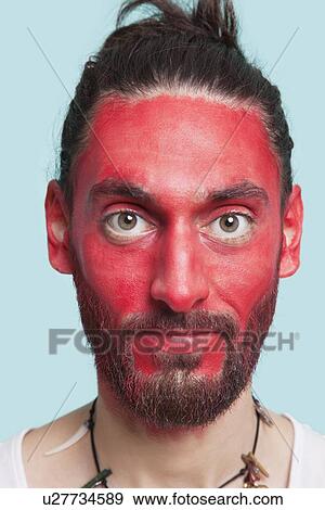 Portrait of young man with red painted face against blue background View Large Photo Image Stock Photo - Portrait of young man with red painted face against blue background. Fotosearch