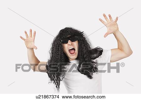 Picture - Portrait of young man with wig and sunglasses shouting against gray background. Fotosearch