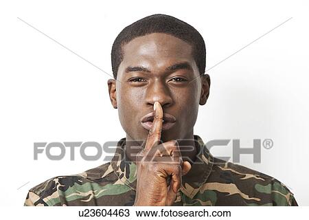 Stock Image - Portrait of young military soldier in camouflage clothing making silent gesture against white background. Fotosearch