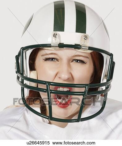 Stock Photography - Portrait of young woman in football uniform screaming against gray background. Fotosearch