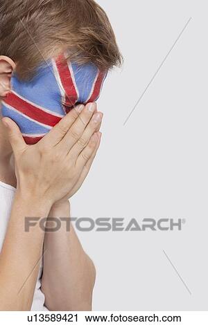 Stock Image - Sad young Caucasian man with British flag painted on face against white background. Fotosearch