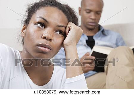 Sad young woman with man reading book in background View Large Photo Image Stock Photo - Sad young woman with man reading book in background. Fotosearch