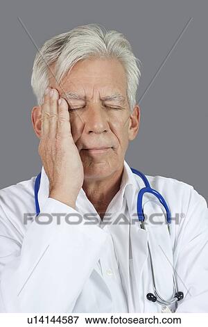 Senior doctor suffering from headache over gray background View Large Photo Image Stock Photo - Senior doctor suffering from headache over gray background. Fotosearch