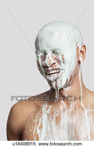 Stock Photography - Shirtless young man with face covered in paint against gray background. Fotosearch