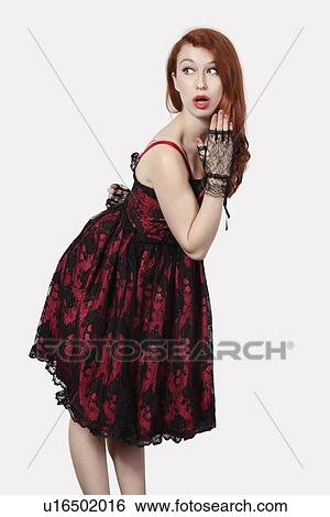 Stock Photograph - Shocked young woman in retro styled lace dress against gray background. Fotosearch