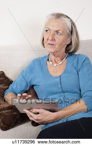 Thoughtful senior woman using digital tablet at home View Large Photo Image Stock Photograph - Thoughtful senior woman using digital tablet at home. Fotosearch