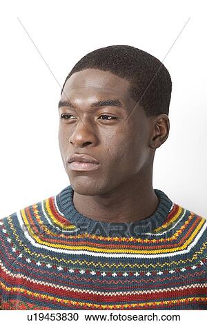 Stock Image - Thoughtful young man in knitwear looking away against white background. Fotosearch