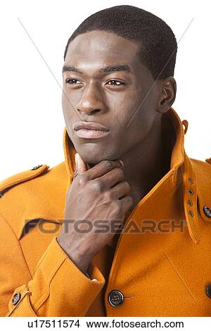 Picture - Thoughtful young man in orange trench coat looking away against white background. Fotosearch