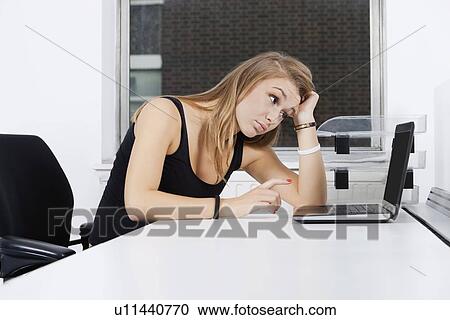 Tired young businesswoman looking at laptop in office View Large Photo Image Stock Image - Tired young businesswoman looking at laptop in office. Fotosearch