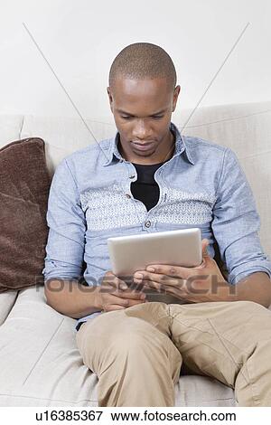 Stock Photo - Young African American man using tablet PC at home. Fotosearch