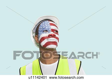 Stock Image - Young architect with American flag painted on face against colored background. Fotosearch